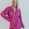 Front view of model wearing the On A Break Top which features fuchsia plisse fabric, ruffled trim, a button-up front with monochromatic buttons, a collared neckline, and long sleeves.