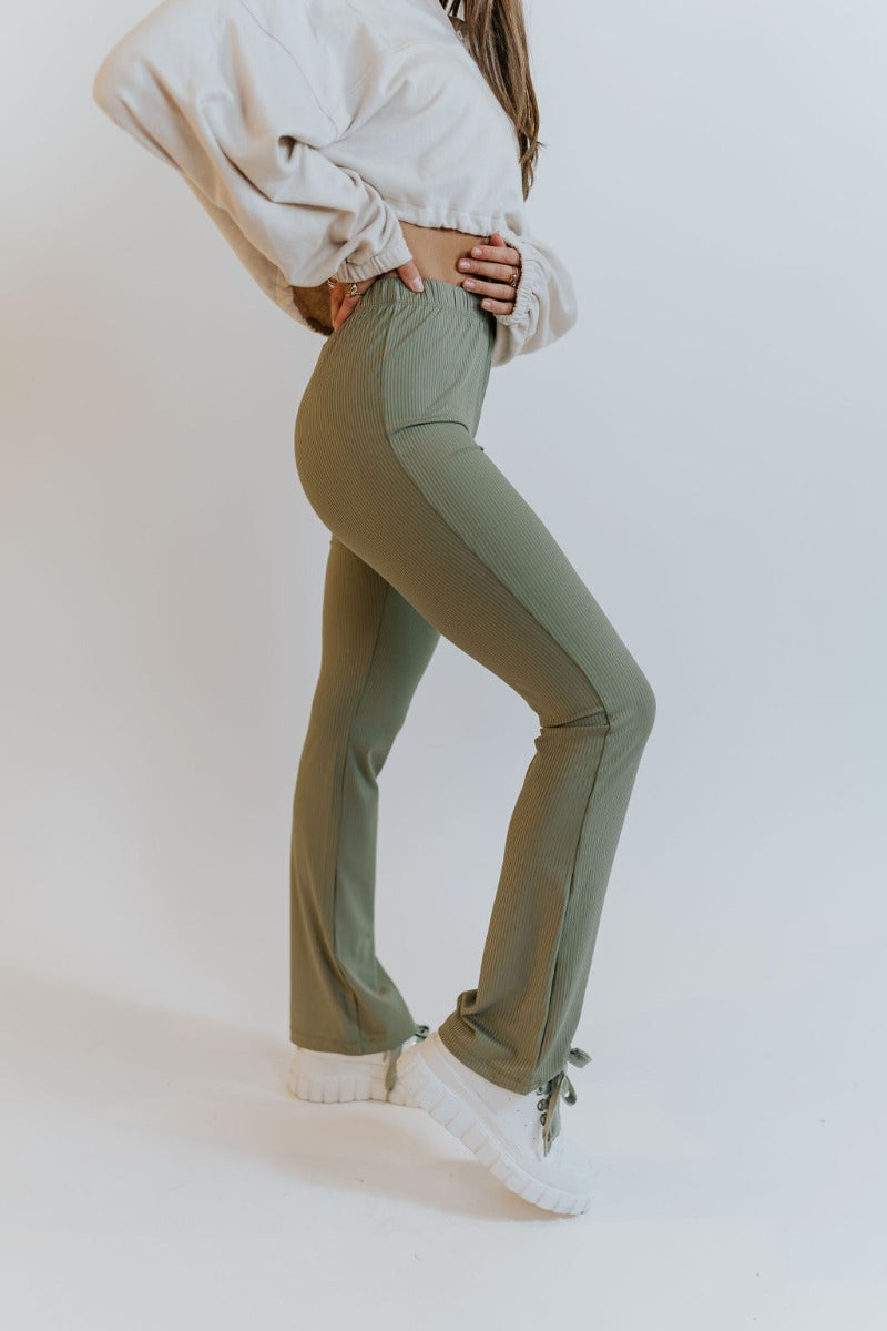 Side view of model wearing the Forget It Ribbed Pants that have olive green ribbed fabric, an elastic waistband, and flared legs.
