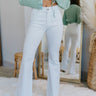 Front view of model wearing the Rooted Denim: Coming In Hot Jeans which features white denim fabric, two front pockets, front zipper and button closure, waistband has belt loops, two back pockets and wide flare leg pant with distressed hem.