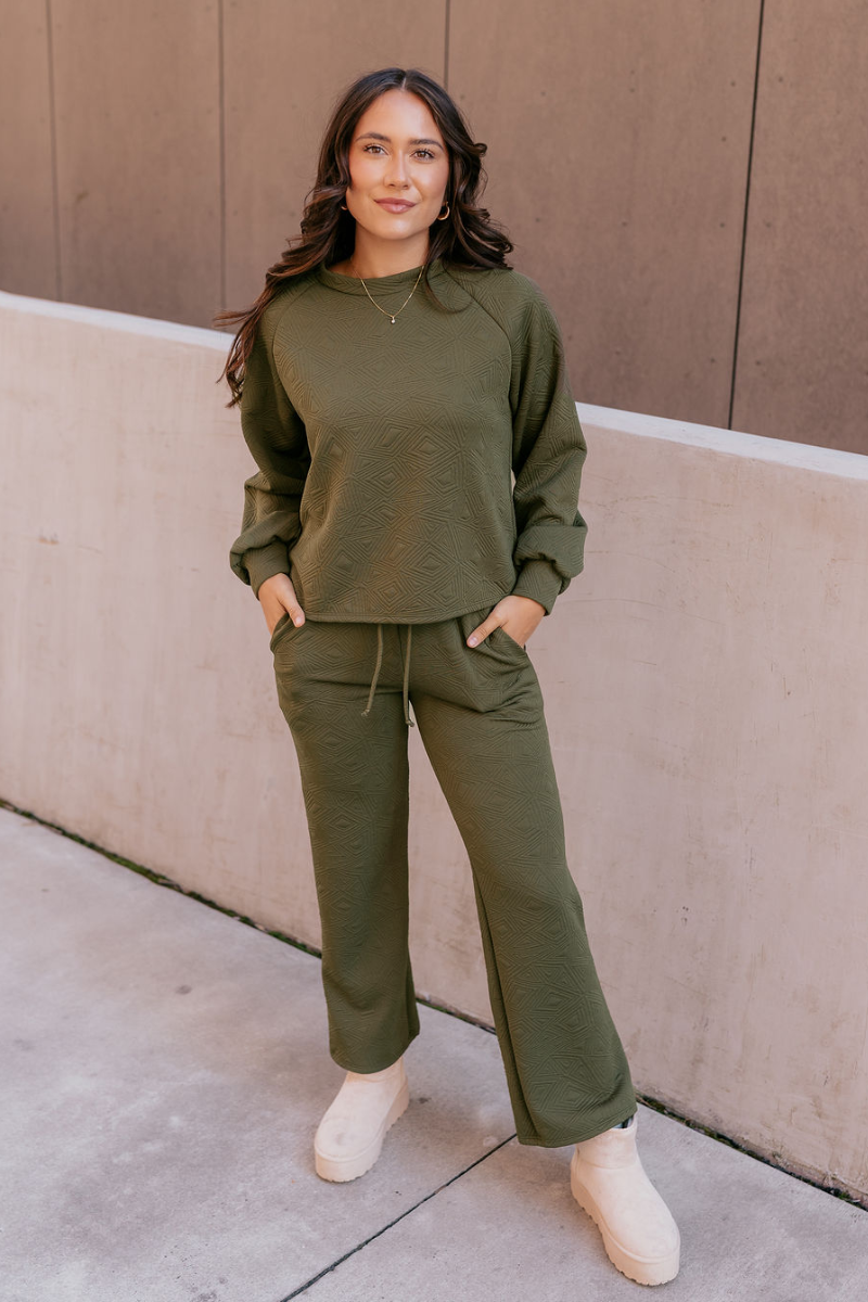 Full body view of model wearing the Aria Olive Green Pattern Lounge Top which features olive green knit fabric, a monochrome geometric quilted pattern, a round neckline, and long balloon sleeves with cuffs.