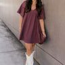 Full body front view of model wearing the Bella Purple Gauze Short Flare Sleeve Dress that has plum gauze fabric, ruffled details, mini length, an elastic waistband, a plunge neckline, a back tie closure, and short flare sleeves.