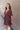 Side view of model wearing the Bella Purple Gauze Short Flare Sleeve Dress that has plum gauze fabric, ruffled details, mini length, an elastic waistband, a plunge neckline, a back tie closure, and short flare sleeves.