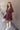 Full body side view of model wearing the Bella Purple Gauze Short Flare Sleeve Dress that has plum gauze fabric, ruffled details, mini length, an elastic waistband, a plunge neckline, a back tie closure, and short flare sleeves.