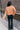 Back view of model wearing the Nina Peach Cropped Long Sleeve Sweater which features peach knit fabric, a ribbed round neckline, dropped shoulders with exposed seams, and long flare sleeves.