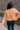 Back view of model wearing the Nina Peach Cropped Long Sleeve Sweater which features peach knit fabric, a ribbed round neckline, dropped shoulders with exposed seams, and long flare sleeves.