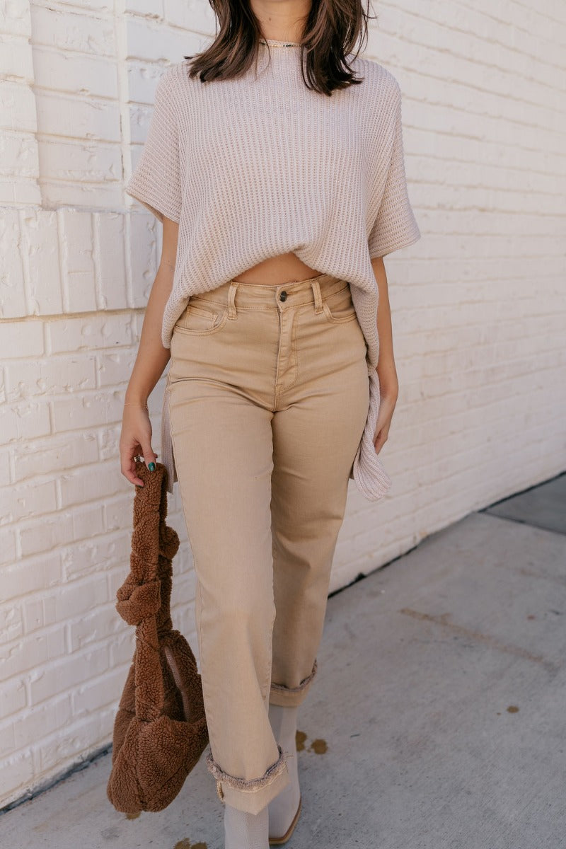 front view of model wearing the Rooted Denim: Morgan Light Mustard Straight Leg Jeans that have pale mustard/brown denim fabric,  pockets, and a frayed hem.