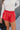 Close front view of model wearing the Kali Red Faux Leather Ruffle Skort that has red faux leather, a ruffle tier design, red shorts lining, and an elastic waistband with a tie closure.