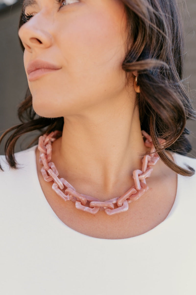 Close up of model wearing the Kendall Pink Chain Link Statement Necklace that has square shaped links with a blush and mauve marble design and a gold adjustable link closure.