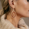 Close side view of model wearing the Nora Gold & Brown Teardrop Earrings that have teardrop shaped pendants linked with two brushed gold layers and one wooden layer with brushed gold hobnail accents.