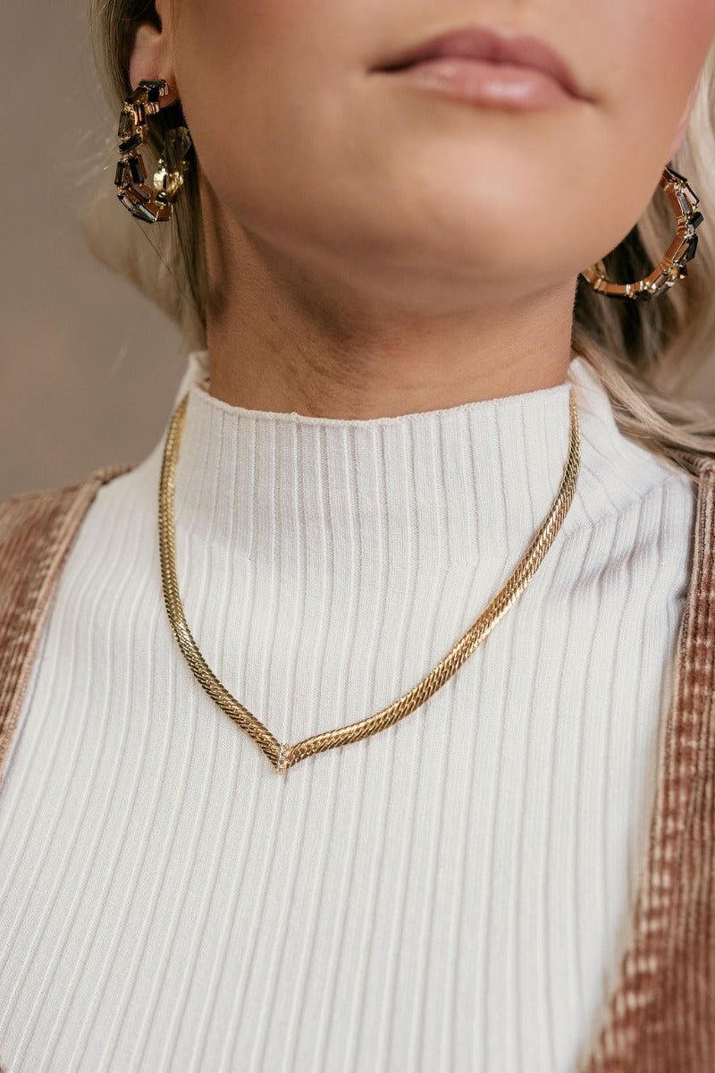 Front view of model wearing the Ella Gold Pointed Herringbone Necklace that has one gold flat herringbone link, a pointed design with clear stones, and an adjustable clasp closure