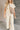 Full body front view of model wearing the Kalani Cream Quilted Pants that have cream fabric, a monochrome geometric quilted pattern, two front pockets, an elastic waist with a drawstring tie, and wide legs.