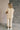 Full body back view of model wearing the Kalani Cream Quilted Pants that have cream fabric, a monochrome geometric quilted pattern, two front pockets, an elastic waist with a drawstring tie, and wide legs.