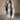 Full body front view of model wearing the Brynn Grey Plaid Longline Shacket that has black, grey, brown and white plaid print, midi length, tortoise buttons, front chest buttoned pockets, a collar, and long sleeves.