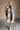 Full body front view of model wearing the Brynn Grey Plaid Longline Shacket that has black, grey, brown and white plaid print, midi length, tortoise buttons, front chest buttoned pockets, a collar, and long sleeves.