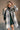 front view of model wearing the Brynn Grey Plaid Longline Shacket that has black, grey, brown and white plaid print, midi length, tortoise buttons, front chest buttoned pockets, a collar, and long sleeves.