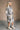 Full body side view of model wearing the Brynn Grey Plaid Longline Shacket that has black, grey, brown and white plaid print, midi length, tortoise buttons, front chest buttoned pockets, a collar, and long sleeves.