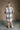 Full body back view of model wearing the Brynn Grey Plaid Longline Shacket that has black, grey, brown and white plaid print, midi length, tortoise buttons, front chest buttoned pockets, a collar, and long sleeves.