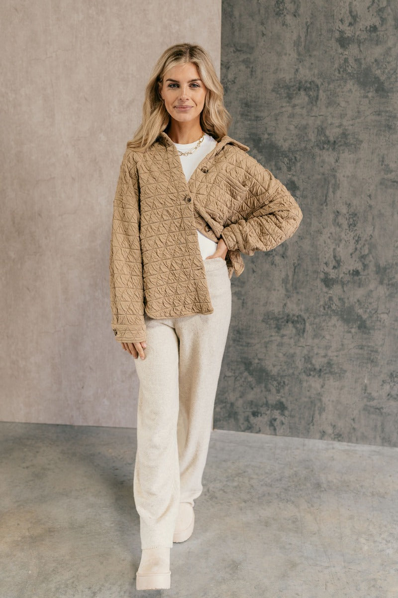 Full body front view of model wearing the Kira Taupe Quilted Shacket that has taupe textured fabric with a quilted pattern, a left front chest pocket, a scooped hem, tortoise buttons, a collar, and long sleeves.