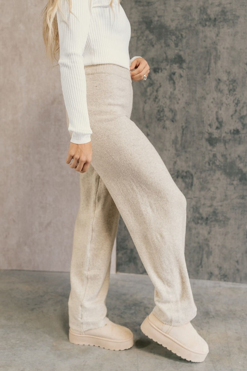 side view of model wearing the Destiny Oatmeal Knit Pants that have oatmeal knit fabric, a ribbed elastic waistband, and wide legs. 