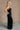 Full body side view of model wearing theElisa Black Satin Cowl Neck Maxi Dress that havs black satin fabric, maxi length,, a cowl neck, adjustable straps, and a back zipper with a hook closure.