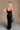Full body back view of model wearing theElisa Black Satin Cowl Neck Maxi Dress that havs black satin fabric, maxi length,, a cowl neck, adjustable straps, and a back zipper with a hook closure.