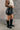 Side view of model wearing the Rosie Black Faux Leather Cargo Skort that have black faux leather, black faux leather shorts lining, two front cargo pockets, and a front zipper with a hook closure.