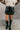 Front view of model wearing the Rosie Black Faux Leather Cargo Skort that have black faux leather, black faux leather shorts lining, two front cargo pockets, and a front zipper with a hook closure.
