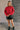 Full body front view of model wearing the Lorelei Red Mock Neck Sweater that has red cable knit fabric, ribbed hem, a high neck with braided details, dropped shoulders and long balloon sleeves.