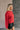 Side view of model wearing the Lorelei Red Mock Neck Sweater that has red cable knit fabric, ribbed hem, a high neck with braided details, dropped shoulders and long balloon sleeves.