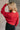 Back view of model wearing the Amara Red Cable Knit Long Sleeve Sweater which features red knit fabric, monochrome cable knit design, ribbed hem, cropped waist, round neckline, dropped shoulders and long sleeves with cuffs.