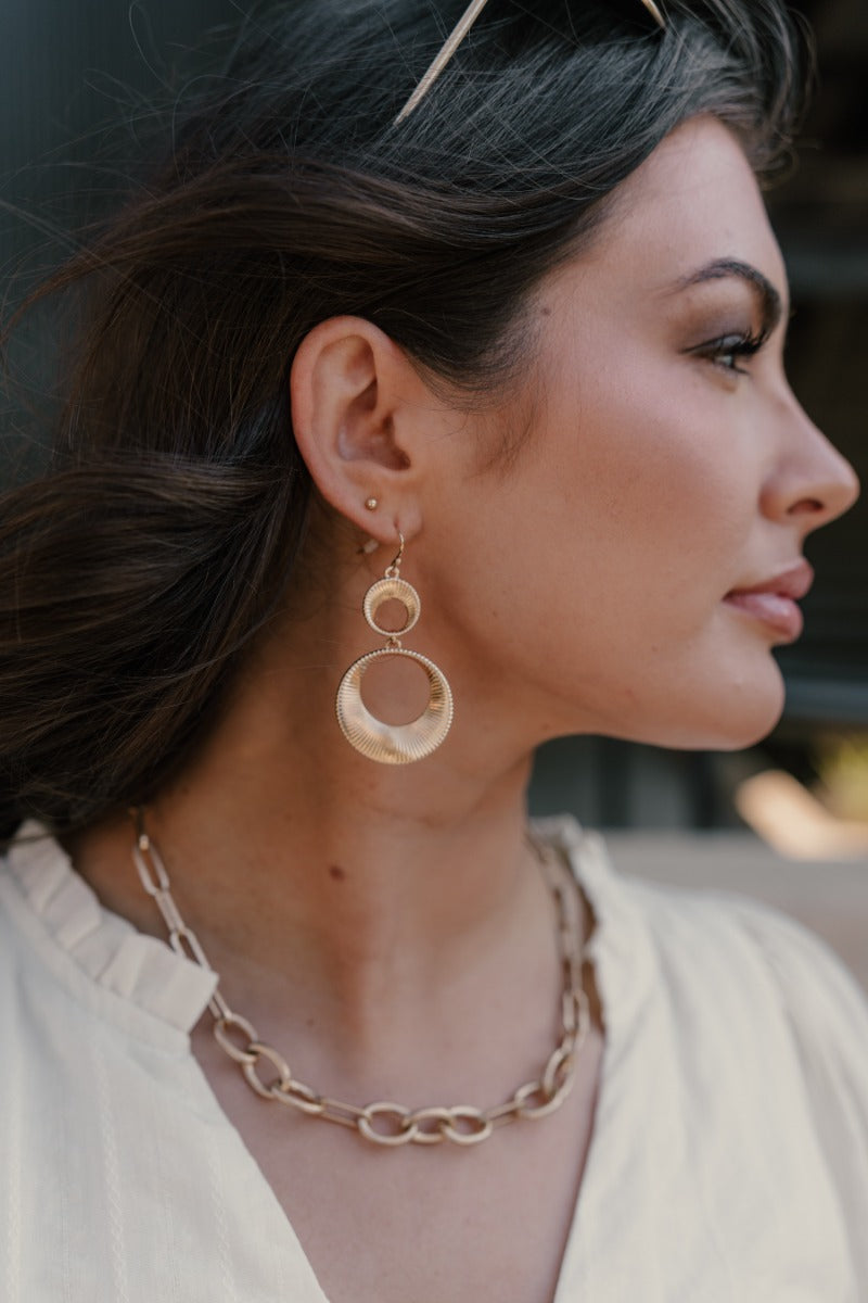 Side view of model wearing the Presley Gold Earrings that feature two gold ribbed open circles linked together.