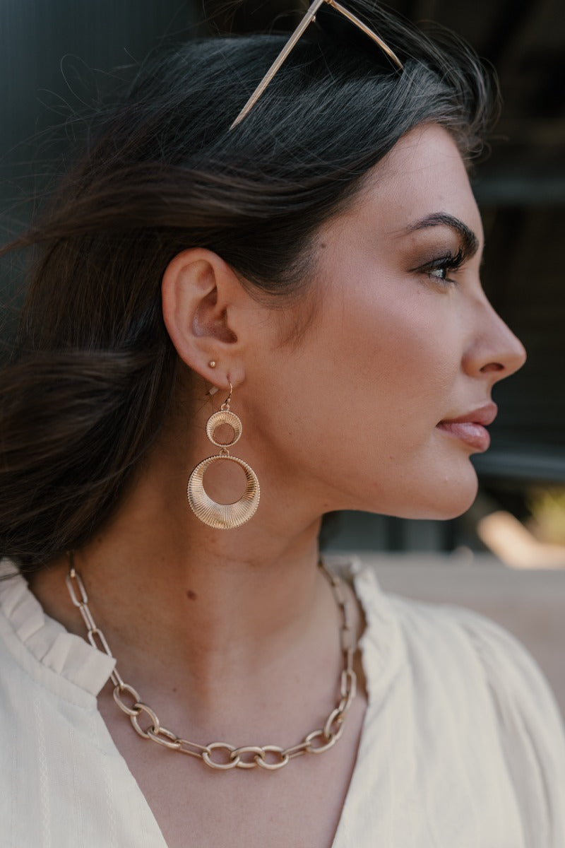Side view of model wearing the Presley Gold Earrings that feature two gold ribbed open circles linked together.
