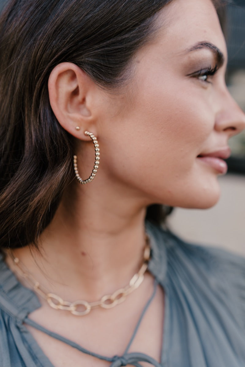 Side view of model wearing the Lila Gold Bead Hoop Earrings that feature open medium hoop with gold beads.