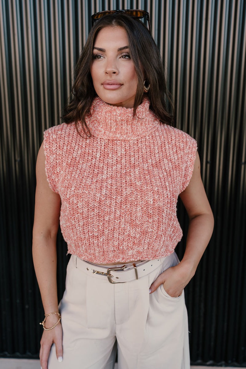 Front view of model wearing the Jordyn Orange & White Sleeveless Turtleneck Sweater which features orange and white cable knit fabric, a cropped waist, a turtleneck neckline, and a sleeveless design.