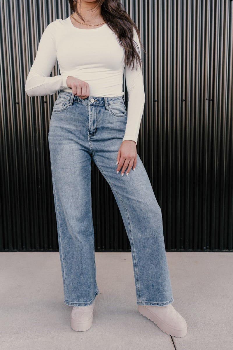 front view of model wearing the Ceros: Daniela Wide Leg Jeans that have medium blue denim fabric, a front zipper, pockets, belt loops and wide legs.