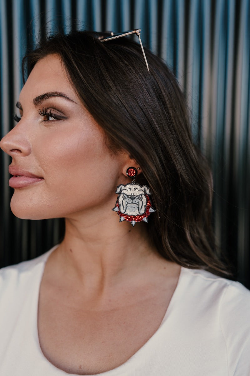 Side view of model wearing the Bulldog Game Day Earrings that feature bulldog face shaped dangle earrings with red and white glitter details.