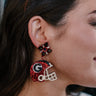 Side view of model wearing that UGA Red & Black Glitter Helmet Earrings that have football helmet shaped earrings, red, white and black glitter details, a Georgia "G" design and a starburst stud design.