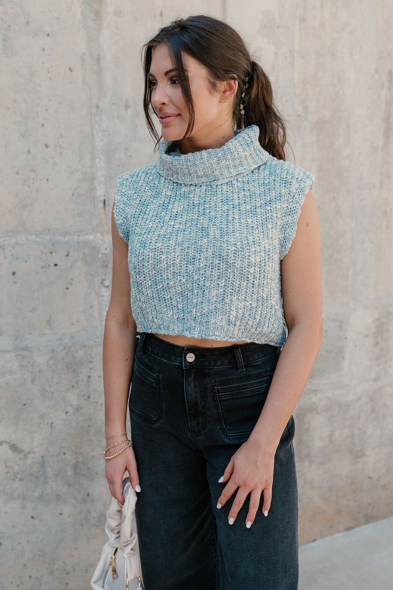 Front view of model wearing the Jordyn Blue & White Sleeveless Turtleneck Sweater which features blue and white cable knit fabric, a cropped waist, a turtleneck neckline, and a sleeveless design.