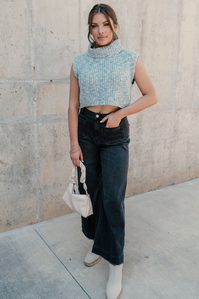 Full body view of model wearing the Jordyn Blue & White Sleeveless Turtleneck Sweater which features blue and white cable knit fabric, a cropped waist, a turtleneck neckline, and a sleeveless design.