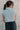 Back view of model wearing the Jordyn Blue & White Sleeveless Turtleneck Sweater which features blue and white cable knit fabric, a cropped waist, a turtleneck neckline, and a sleeveless design.