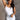 Front view of model wearing the Vera White Sleeveless Bodysuit which features white knit fabric, v-neckline, adjustable spaghetti straps, sleeveless and thong bottom with button snap closure.