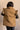 Back view of model wearing the Esme Chartreuse Ruffle Puffer Vest, that has olive puffer fabric, button up closures, two front pockets, high collar neck, short sleeves with ruffles. Worn unbuttoned over cream dress.