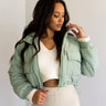 front view of model wearing the Mckinley Mint Cropped Puffer Jacket that has mint green puffer fabric, a cropped waist, a front zipper with snaps, a hood, and long sleeves.
