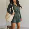 Full body front view of model wearing the Ezra Grey Green Long Sleeve Romper that has grey green knit fabric, pockets, an elastic waist, a front zipper, a hood, a skirt with fitted shorts , and long sleeves.