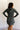 Back view of model wearing the Ezra Grey Green Long Sleeve Romper that has grey green knit fabric, pockets, an elastic waist, a front zipper, a hood, a skirt with fitted shorts , and long sleeves.