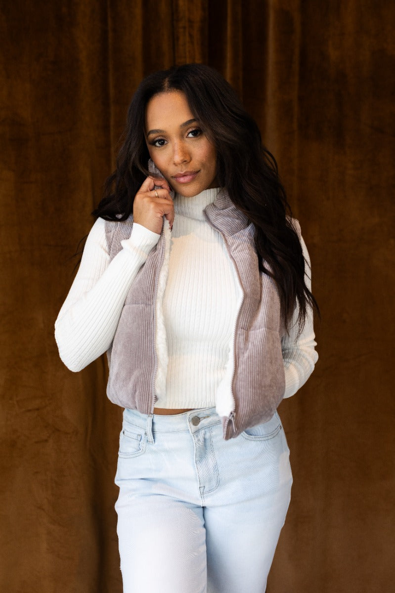 front view of model wearing the Aliana Grey Corduroy & Sherpa Puffer Vest that has grey corduroy fabric, a drawstring hem, sherpa lining, a monochrome zipper, and a high neckline.