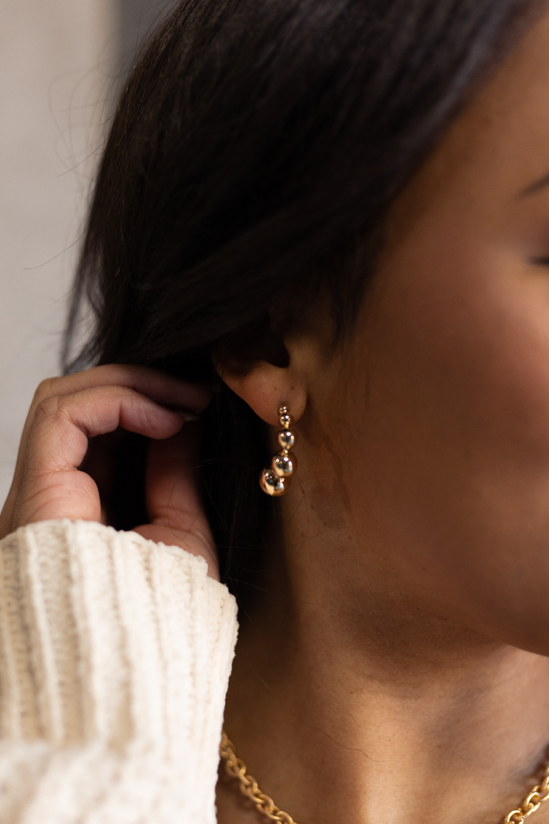 Close up view of model wearing the Aurora Gold Bead Scooped Earring which features open hoops with small, medium and large gold beads.