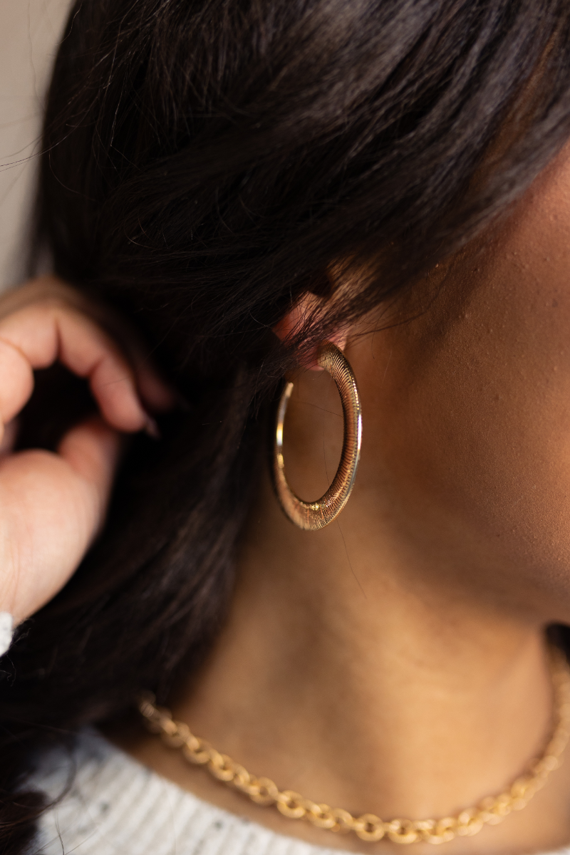 Close up view of model wearing the Elena Gold Textured Open Large Hoop which features large gold flat band open hoops.