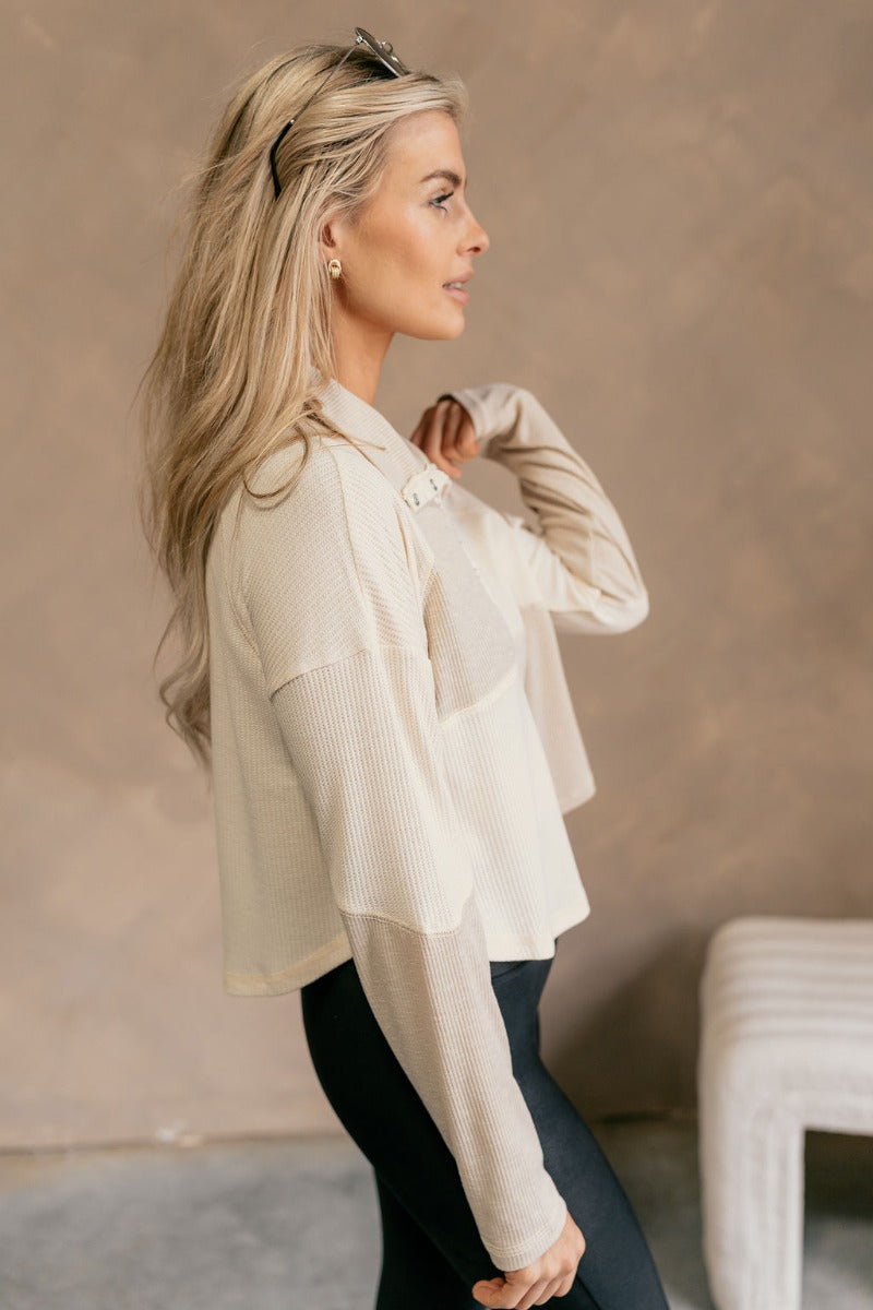 Side view of model wearing The Julia Cream Color Block Thermal Top features cream and taupe waffle knit fabric, color block pattern, quarter button up closure, high neckline, dropped shoulders and long sleeves.