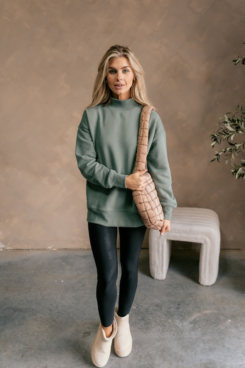 Front view of model wearing The Jennifer Sage Mock Neck Sweatshirt features sage green knit fabric, two front slit pockets, ribbed hem, high neckline and long sleeves with cuffs.